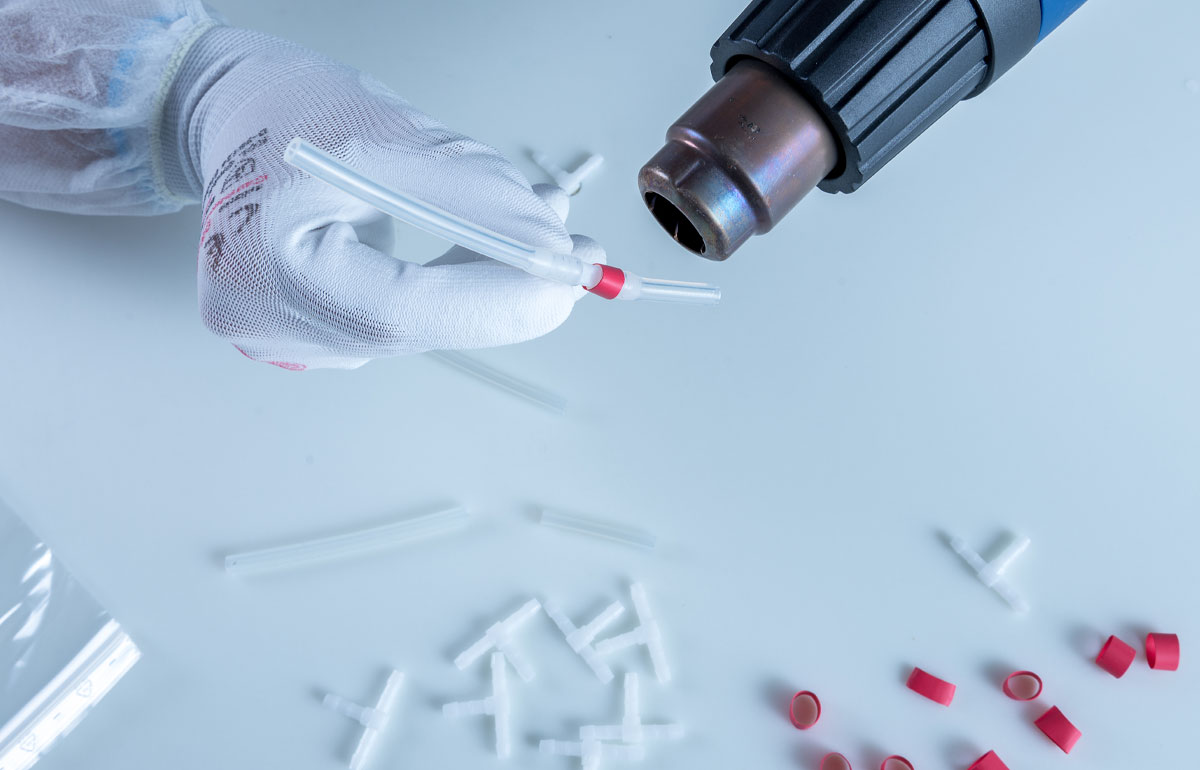 Hände im Detail, die mit einem Heißfön zwei Schläuche, mit Hilfe einer Dichtung, zusammenfügen.