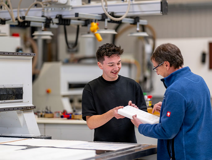 Azubi lässt sich vom Arbeitgeber Papiere unterschreiben. Sie stehen an einem Werktisch.